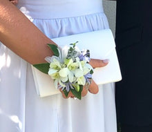 Load image into Gallery viewer, A person wearing a white wrist corsage made of flowers, attached to a white fabric possibly a dress.