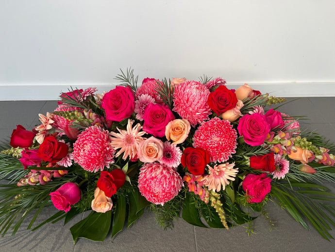 long and low large spray of Fresh flowers , can sit on a casket or table. this picture has bright roses,disbuds,gerberas,tulips,snapdragons,and foliage measuresaround 110cm in lenghth,approx30cm in width and approx 17cm in height