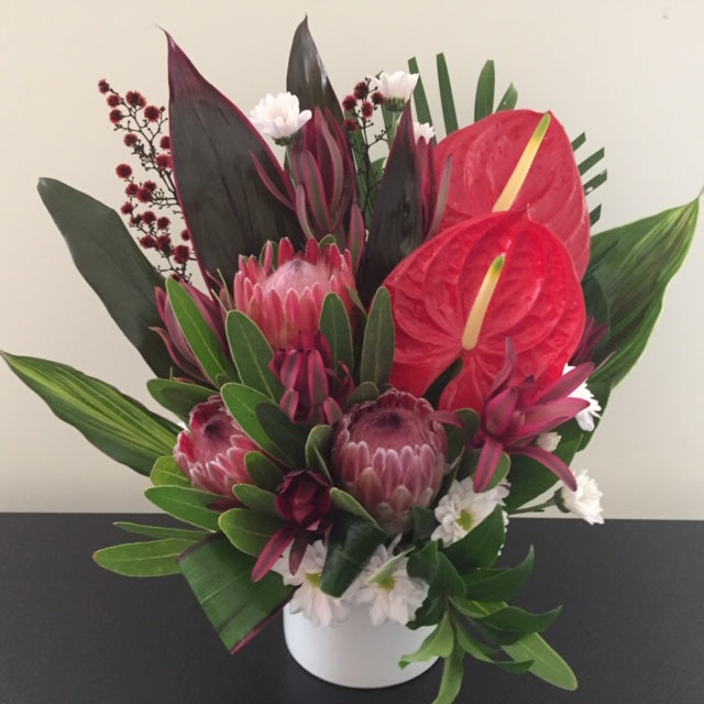 Flowers designed in a container,tropical leaves,anthurium,proteas or native substitute.bright,textural,stylish flower arrangement.
