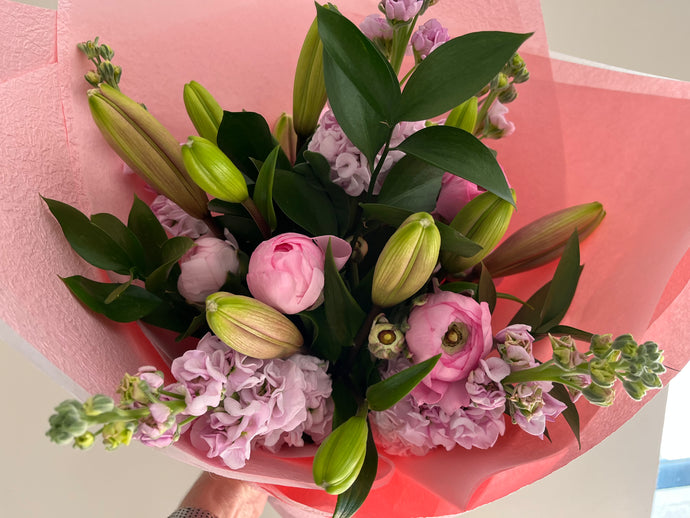 A bouquet of flowers with a variety of colors including pink and green, wrapped in a pink paper.